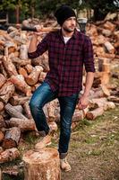 He loves working with wood. Full length of handsome young forester carrying axe on his shoulders and looking away while standing outdoors photo