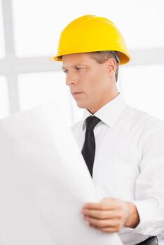 Architect with blueprint. Confident senior man in formalwear and hardhat holding a blueprint and looking at it photo