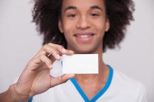 Your text here. Cheerful African teenager holding plastic card and smiling at camera while standing isolated on grey background photo