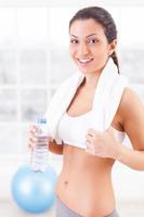 Getting refreshed. Beautiful young woman in sports clothing holding a bottle with water and smiling at camera photo