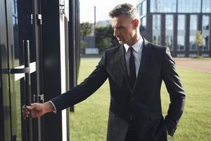 Confident mature businessman opening the door of business centre photo