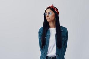 Attractive young woman in bandana looking away while standing against grey background photo