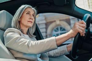 Mature beautiful woman in smart casual wear looking away while driving car photo