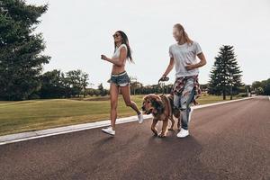 Great day together. Full length of beautiful young couple running with their dog while spending time outdoors photo