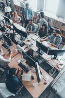 Successful young team at work. Top view of group of young business people in smart casual wear working together while sitting at the large office desk photo