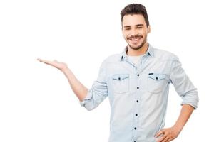 Copy space on his hand. Handsome young man in shirt looking at camera and holding copy space while standing against white background photo