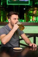 bebiendo cerveza fresca. un joven pensativo bebiendo cerveza y mirando hacia otro lado mientras estaba sentado en el bar foto
