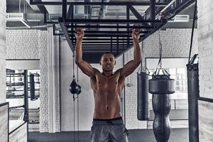 Pushing hard to win. Handsome young African man looking at camera and doing pull-ups while exercising in the gym photo