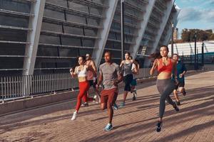 toda la longitud de los jóvenes en ropa deportiva corriendo juntos al aire libre foto