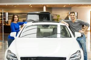 feliz con su coche nuevo. feliz pareja joven de pie a ambos lados del coche sonriendo a la cámara foto