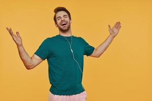 Handsome young man in headphones gesturing and smiling while standing against yellow background photo