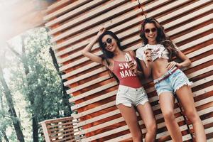 Best friends. Two attractive young women smiling and eating ice cream while standing against the wooden wall outdoors photo