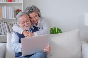 senior husband and wife  sit on sofa look at computer notebook are happy photo