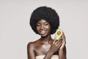 Portrait of beautiful young African woman holding avocado and smiling photo