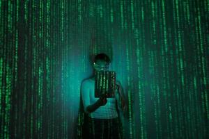 Woman in futuristic glasses using digital tablet against dark background with green symbols photo