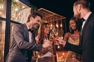 grupo de personas en ropa formal brindando con champán y sonriendo mientras pasan tiempo en una fiesta de lujo foto