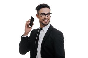 siempre en contacto un joven apuesto con traje completo hablando por teléfono inteligente y mirando hacia otro lado mientras se enfrenta a un fondo blanco foto