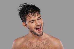 Feeling free to do anything. Good looking young man keeping mouth open and eyes closed while standing against grey background photo