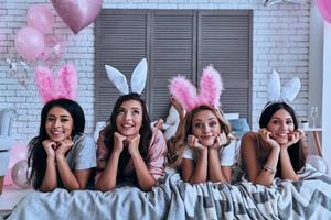 bellezas puras. cuatro atractivas mujeres jóvenes con orejas de conejo sonriendo mientras están acostadas en la cama foto