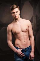 Confident in his perfect body. Handsome young muscular man posing while standing against metal background photo