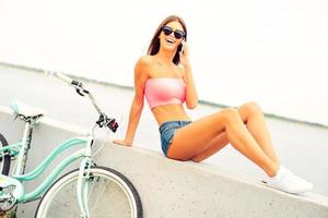 Good talk with friend. Beautiful young smiling woman talking on the mobile phone while sitting on parapet near her bicycle photo