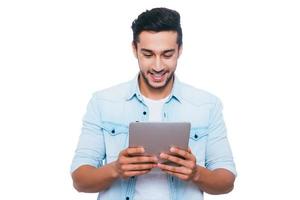 Examining his brand new gadget. Handsome young Indian man holding digital tablet and looking at it with smile while standing against white background photo