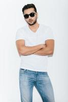 Cool and handsome. Handsome young Indian man in sunglasses keeping arms crossed and looking at camera while standing against white background photo