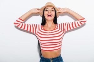 Chica miedosa. mujer joven alegre ajustando su sombrero mientras está de pie contra el fondo blanco foto