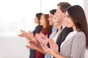 People applauding. Side view of group of cheerful young people standing in a row and applauding to someone photo