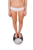 Woman with weight scale. Top view of young slim woman in underwear standing on weight scale while isolated on white photo