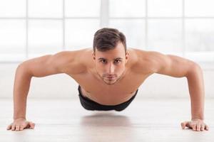 Lagartijas. joven musculoso haciendo flexiones y mirando a la cámara foto