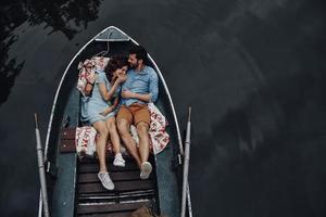 Nice time together. Top view of beautiful young couple embracing and smiling while lying in the boat photo