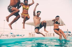 tiempo para divertirse en la piscina. grupo de hermosos jóvenes que se ven felices mientras saltan juntos a la piscina foto