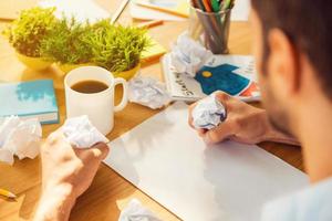 It is always hard to start. Close-up rear view of man smashing pieces of paper while sitting at his working place photo