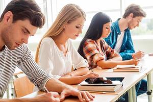 Concentrated on exam. Group of young students writing something in their note pads while sitting in a row at their desks photo