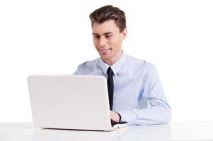 Businessman working on laptop. Handsome young man in shirt and tie sitting at the table and working on laptop while isolated on white photo