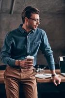 Good looking young man in smart casual holding cup and looking away photo