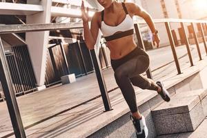 siempre en gran forma. mujer joven moderna en ropa deportiva corriendo mientras hace ejercicio al aire libre foto