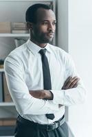 Time to make decision. Handsome young African man keeping arms crossed and looking somewhere while standing in creative office photo