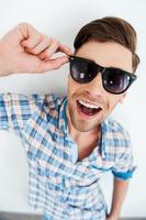 Cool and trendy. Top view of cheerful young man adjusting eyewear while standing against white background photo