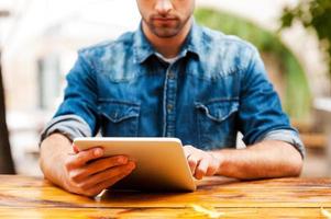 The whole world in one touch. Cropped image of young man working on digital tablet while sitting at the wooden table outdoors photo
