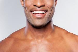 Man with perfect smile. Cropped image of young shirtless African man smiling while standing against grey background photo
