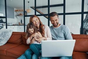 hermosa familia juguetona con una niña que se une y sonríe mientras usa una laptop en casa foto