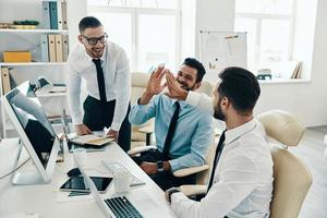 High five for success. Group of young modern men in formalwear smiling while working in the office photo