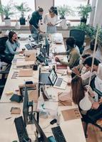 Top view of young modern people in smart casual wear communicating and using modern technologies while working in the office photo