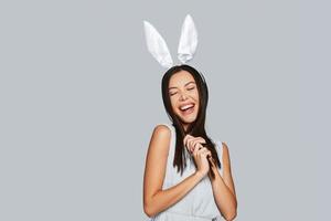 belleza juguetona. bella joven asiática con orejas de conejo sonriendo mientras se enfrenta a un fondo gris foto