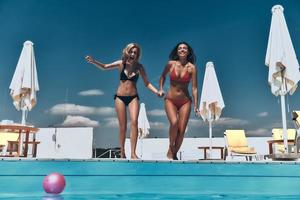 Full length of two attractive young women in bikini preparing to jump into the pool photo