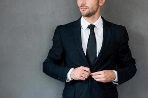Everything should be perfect. Cropped image of confident young businessman adjusting his jacket and while standing against grey background photo