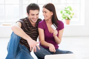 Internet shopping. Beautiful young couple working on laptop together while woman holding a plastic card and smiling photo