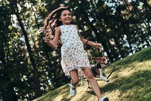 jugando con su perro. toda una linda niña jugando con su perro y sonriendo mientras corre al aire libre foto